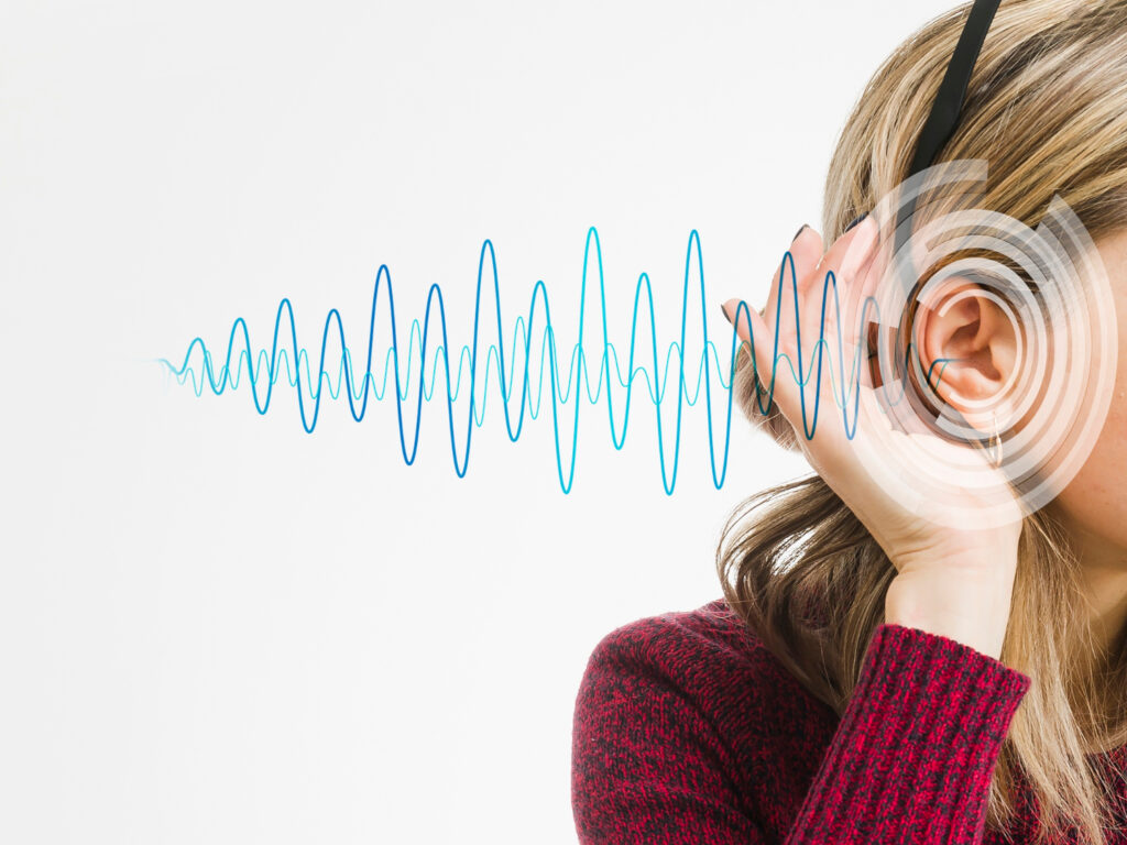 Una mujer se acerca una mano a su oreja, de la que salen ondas de sonido que fluctuan en el aire.